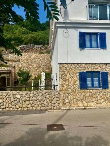 a building with blue windows and a stone wall at Apartman Anton in Stara Baška