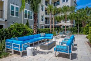 Gated Resort Style 2BR - KING Bed, Pool Views, SPA Hot Tub, Gym, WiFi, Wash & Dry, AC, Elevators, Starbucks, EV CHRG Station, Free Parking, Pets -- IDEAL FOR Medical, Business, Relocation, Long Stays - by Moffitt Cancer Ctr, USF, River Hills Country Club في تامبا: فناء به أرائك وطاولات زرقاء وأشجار نخيل