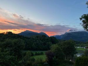 a sunset over the mountains with a field and trees at Shelby's Home in Heimstad +35 photos