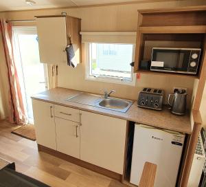 eine kleine Küche mit Spüle und Mikrowelle in der Unterkunft Oxley Retreat, West Sands, Seal Bay Resort in Selsey