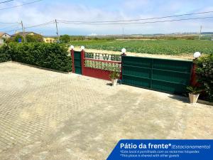 a green fence with a red gate in front of a field at W.H.House in Atouguia da Baleia