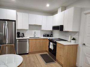 a kitchen with white cabinets and stainless steel appliances at Brand New Deluxe 2 Bedroom Suite with AC & Den in Calgary