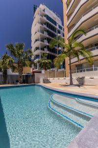 a swimming pool with palm trees and a building at Wyuna Beachfront Holiday Apartments in Gold Coast