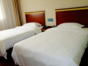 two beds in a hotel room with white sheets at GreenTree Inn ShanDong JiNan Bus Terminal Station Express Hotel in Jinan