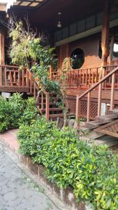 a house with a wooden staircase and some green bushes at Ruean Mai Chai Khlong in Amphawa