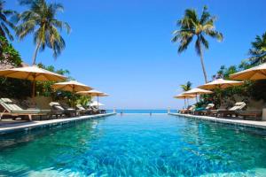 a swimming pool with chairs and umbrellas and the ocean at Raveena 1 BR Classic Garden Room Double ZN139 in Mangsit