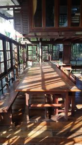 a long wooden table in a room with windows at Ruean Mai Chai Khlong in Amphawa