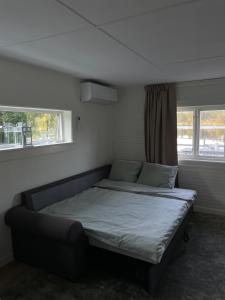 a bed in a room with two windows at Stuga med strandtomt i Smålands natursköna miljö in Vaggeryd