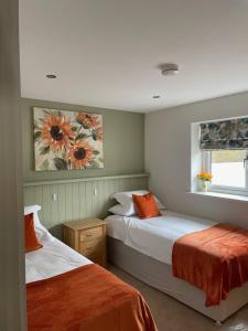 a bedroom with two beds with orange pillows and a window at Sunny Bank in Holsworthy