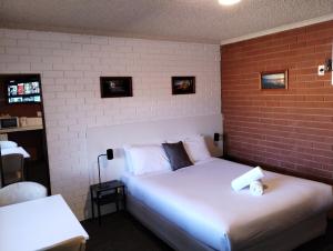 a bedroom with a white bed with a brick wall at Junction Motel Wagga in Wagga Wagga
