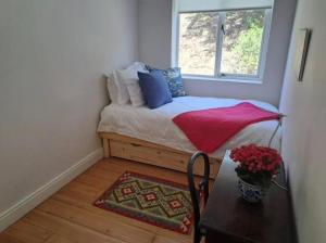 a bedroom with a bed with a table and a window at Little Penguin in Simonʼs Town