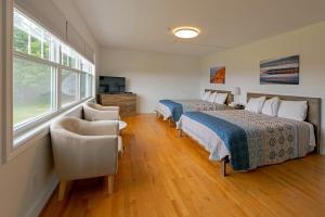 a bedroom with two beds and a chair and a window at Auberge Doucet Inn in Chéticamp