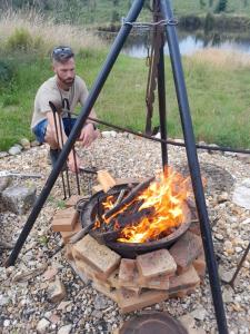 a man is cooking food over a fire at Cuckoo Lake Forest Cabin in Saint-Vincent-Jalmoutiers