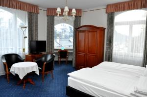 a room with a bed, chair, desk and television at Soldanella in St. Moritz