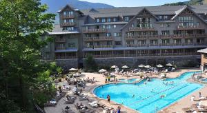 a large hotel with a swimming pool and people sitting around it at Ski in Ski out 4 Bedroom Spruce Peak Lodge Luxury Mountain Cabin By Stowe Mountain Rentals in Stowe