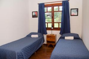 a bedroom with two beds and a window with blue curtains at Casa La Selva in Sierra de los Padres