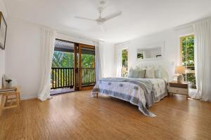 a white bedroom with a bed and a balcony at Treetops Retreat by The Beach in Suffolk Park