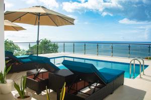 a swimming pool with chairs and an umbrella and the ocean at Villa Vino Lucia in Marigot Bay