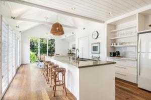 a kitchen with white cabinets and a bar with stools at Frangipani Cottage - Belle Escapes Byron Bay | Winter Escape Deal | Stay Longer & Save | 1 June – 31 August in Byron Bay