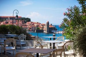 a patio with tables and chairs and a view of the water at Hotel Le Bon Port in Collioure