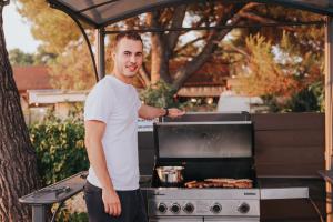 een man die voor een grill staat bij Mobile House Pirovac Kamp Kerido in Pirovac