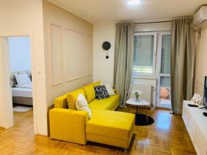 a living room with a yellow couch and a bed at Apartman Hana2 in Sombor