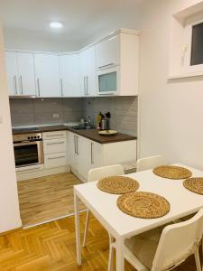 una cucina con mobili bianchi, tavolo e sedie di Apartman Hana2 a Sombor