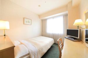 a hotel room with a bed and a desk with a television at Kofu Washington Hotel Plaza in Kofu