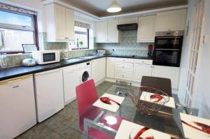 a kitchen with white cabinets and a table with red chairs at Potter's House Coventry in Foleshill