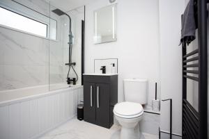 a white bathroom with a toilet and a bath tub at Modern Interior Spacious Four Bedroom Apartment in Westoe