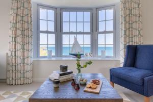 a living room with a table and a blue chair and windows at Sandpipers, Port Isaac Bay Holidays in Port Isaac