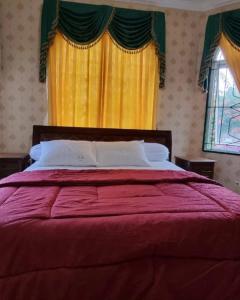 a bedroom with a bed with a red comforter and yellow curtains at Villa Kota Bunga AA2-11 in Cikundul