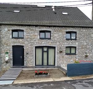 a stone house with a black door and some red flowers at La Grange de David gîte de standing 5 ch 5 sdb - Access-i in Hamoir