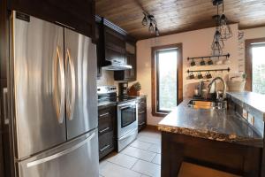 a kitchen with a stainless steel refrigerator and a sink at Au Grand Merisier : Chalet alpin in Petite-Rivière-Saint-François +7 photos