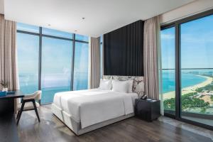 a bedroom with a bed and a desk and windows at Awaken Da Nang Hotel in Danang