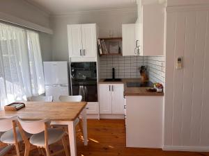 Una cocina con gabinetes blancos y una mesa y sillas. en Nest - charming, comfortable coastal villa, en Port Fairy