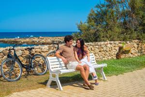 a man and woman sitting on a bench by the beach at Pietrablu Resort & Spa - CDSHotels in Polignano a Mare