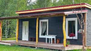a black house with a porch and a table on a deck at aTelpa Namiņš Latgalē in Adamova