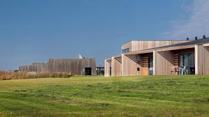 a house on a grassy field with a building in the background at Musholm Holiday, Sport & Conference in Korsør