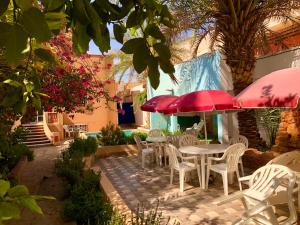 a patio with tables and chairs and red umbrellas at Le Garden Ghardaia in Ghardaïa