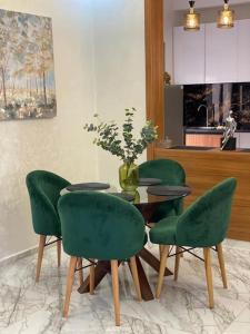 une table avec quatre chaises vertes et un vase avec des fleurs dans l'établissement Appartement de plage - Dahomey Beach - RDC, à Bouznika