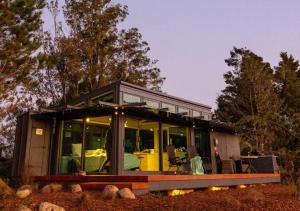 a small house with large glass windows in a field at Ruru PurePod in Waikino +7 photos