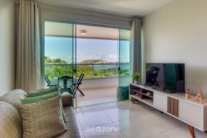 a living room with a tv and a large window at Apto vista p/ rio c/ varanda - Pontal BCL402 in Ilhéus