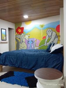 a bedroom with a blue bed with a painting on the wall at Hostal Camino Salinero in Zipaquirá