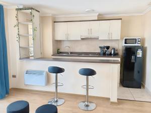 a kitchen with white cabinets and two stools in front of a counter at Amplio y Cómodo departamento in Temuco