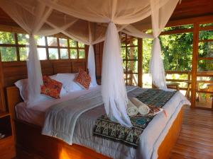 a bedroom with a canopy bed with pillows at VANAYA wooden Lodges in Lush Garden in Pemuteran