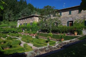 um jardim em frente a um edifício com arbustos e árvores em Badia a Coltibuono Wine Resort & Spa em Gaiole in Chianti