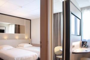 a hotel room with two beds and a mirror at Brit Hotel Nantes La Beaujoire Parc Expo in Nantes