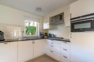 Una cocina blanca con gabinetes blancos y una ventana. en Villapark Kamperfoelie 77, en De Koog 6 fotos más