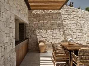 un patio con tavolo e sedie e un muro di pietra di Esthesis Beachfront Villas, with Heated Pool, By ThinkVilla a Alykes